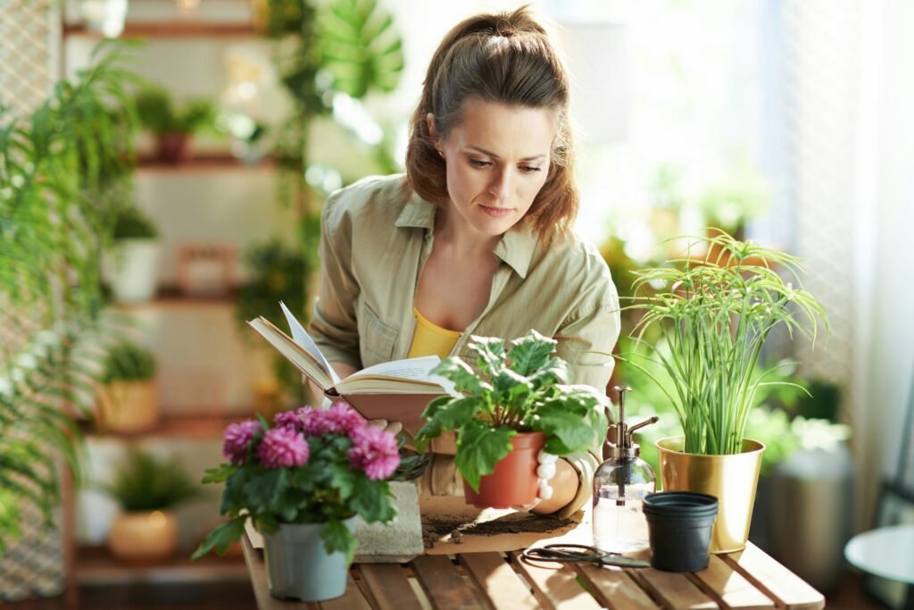 Mulher segurando vaso de planta e consultando um livro de jardinagem, em busca de soluções para cuidar melhor das plantas.