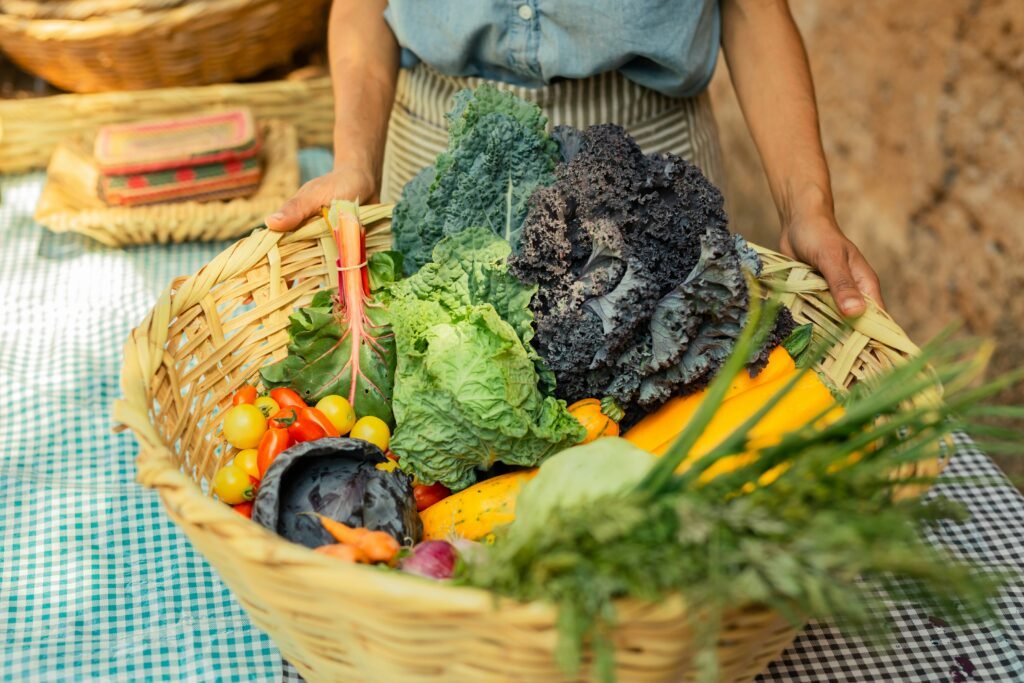 Cesto de vime cheio de hortaliças frescas, como couve, alface, abobrinha, tomates e outros vegetais coloridos, representando a colheita de uma horta caseira.