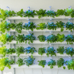 Horta vertical hidropônica com tubos de PVC brancos, cultivando alface, temperos e verduras sob luz artificial em ambiente interno.