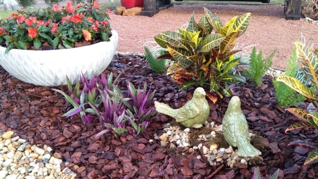 canteiro decorado em jardim para quintal pequeno com flores coloridas, folhagens variadas e esculturas de pássaros de cerâmica