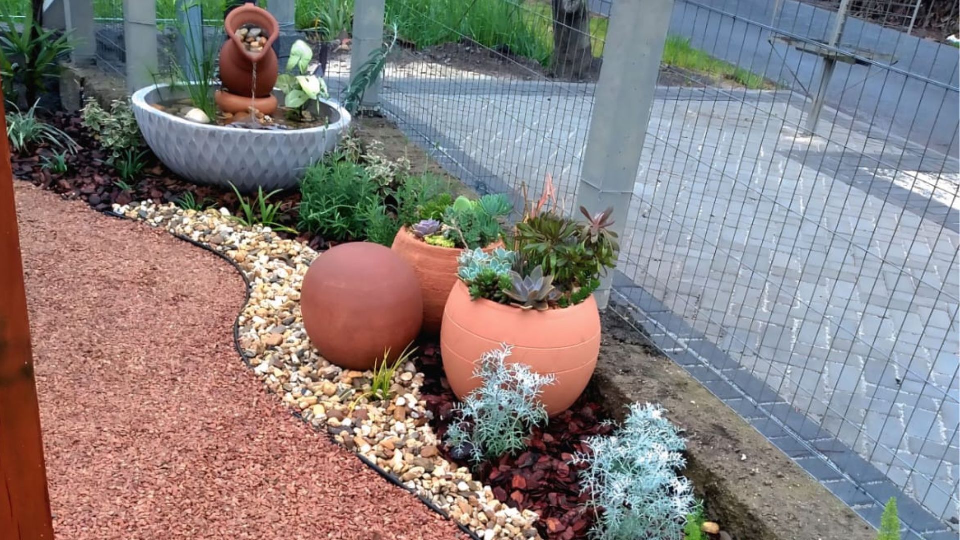 jardim para quintal pequeno com fonte decorativa de cerâmica, vasos com suculentas e caminho de pedriscos