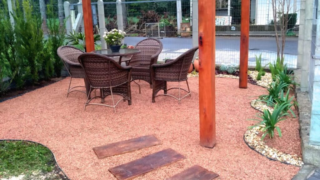 jardim para quintal pequeno com pergolado de madeira, mesa redonda e cadeiras de fibra sintética sobre piso de pedrisco