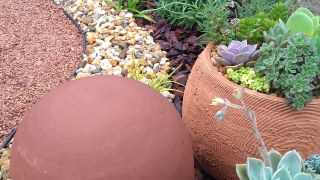 detalhe de jardim para quintal pequeno com vaso de cerâmica cheio de suculentas e caminho de pedriscos