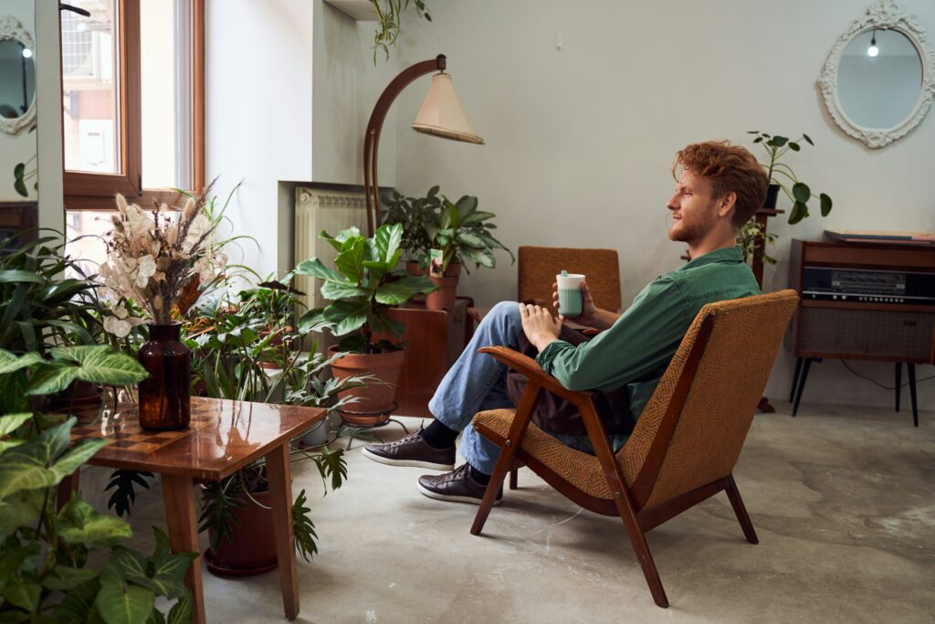 Homem relaxando em sala decorada com diversas plantas de interior em vasos, criando um ambiente aconchegante e natural.