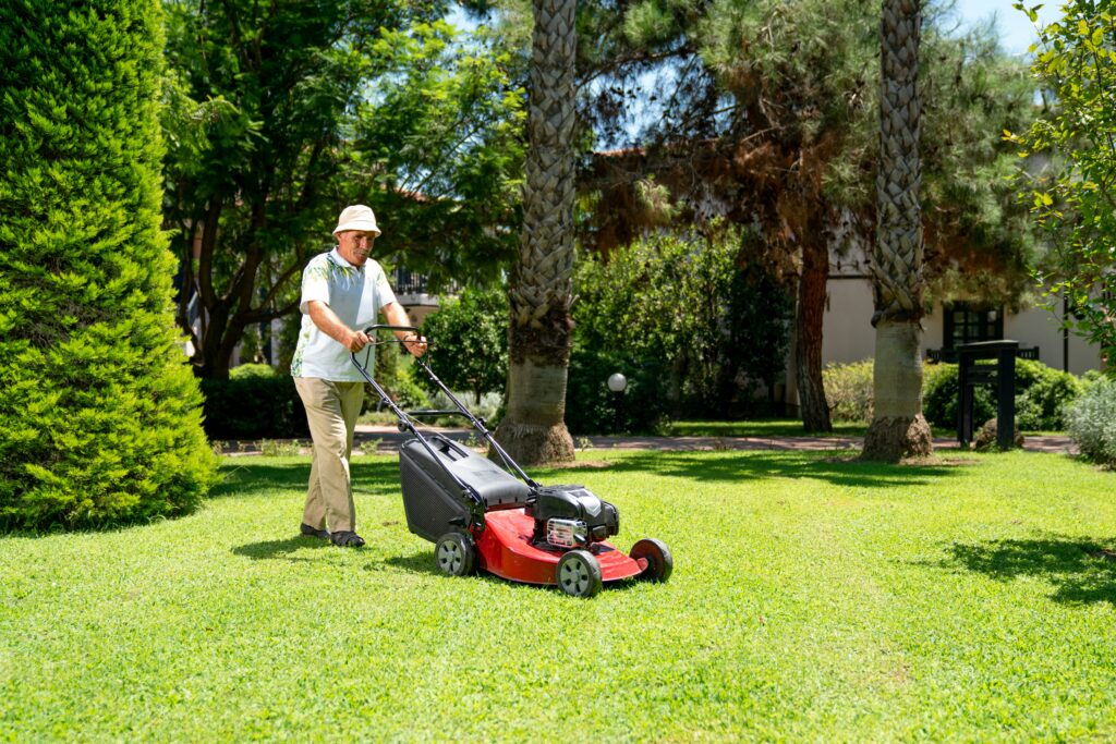 Homem cortando a grama de um jardim bem cuidado com cortador elétrico.
