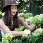 Mulher cuidando de flores verdes em jardim, finalizando os cuidados com as plantas