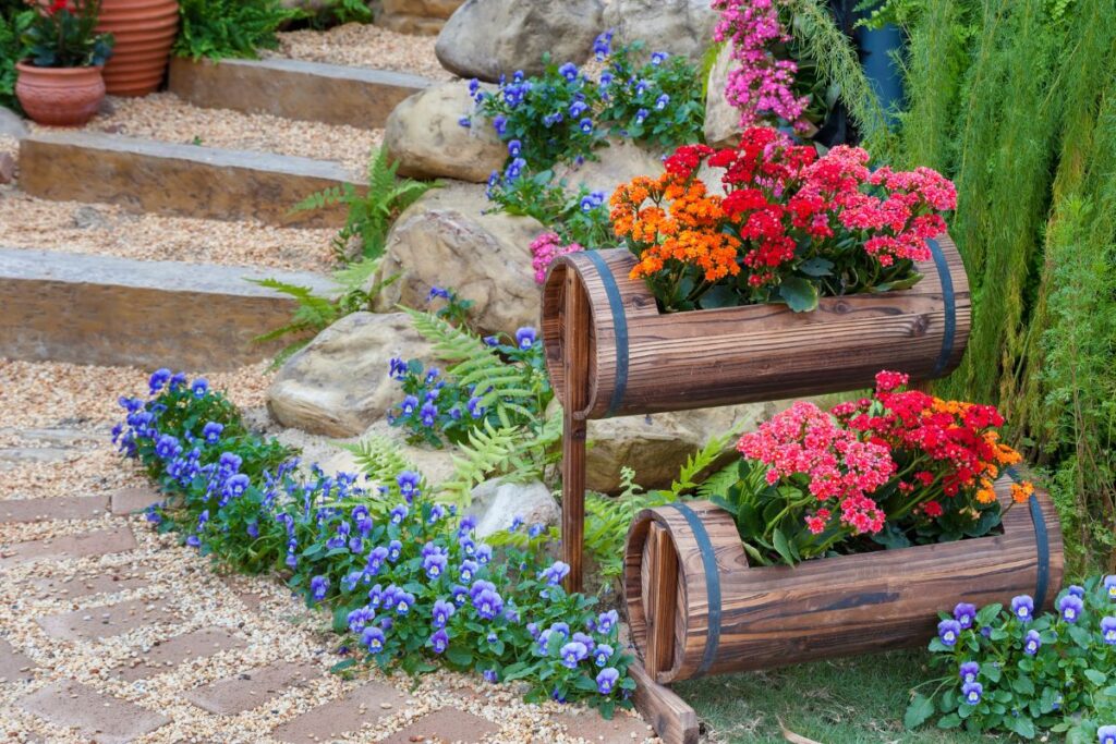 vasos rústicos de madeira com flores coloridas em jardim decorado com pedras e plantas ornamentais