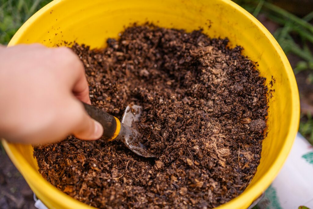 Pessoa misturando solo orgânico em balde amarelo com pá de jardinagem