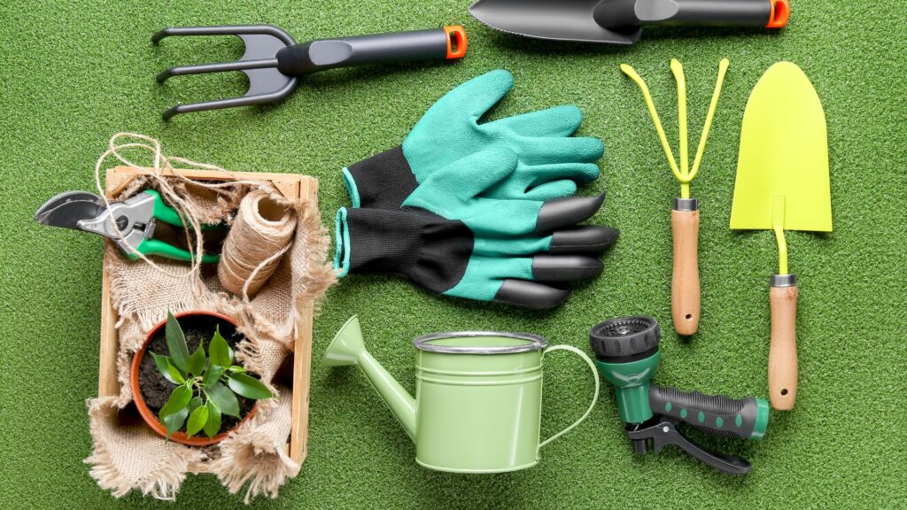 Kit básico de ferramentas de jardinagem com luvas, regador, tesoura de poda e pás sobre grama artificial.