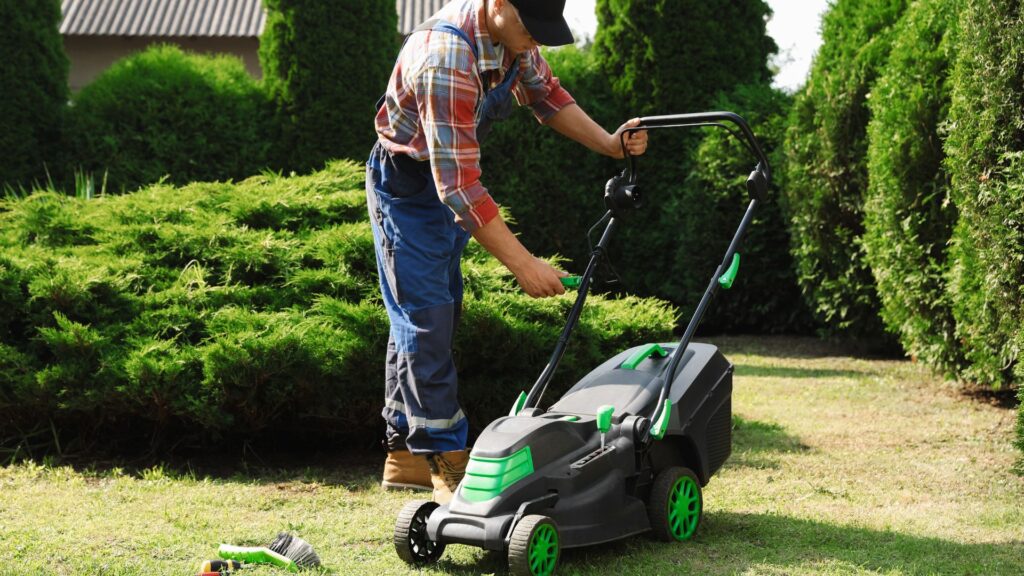 Homem ajustando cortador de grama com coletor em jardim residencial.