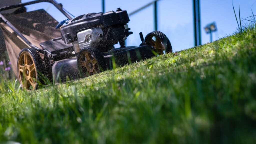 Cortador de grama autopropelido em funcionamento em terreno inclinado, mostrando a tração das rodas e a eficiência do cortador de grama para terrenos irregulares com sistema de autopropulsão.