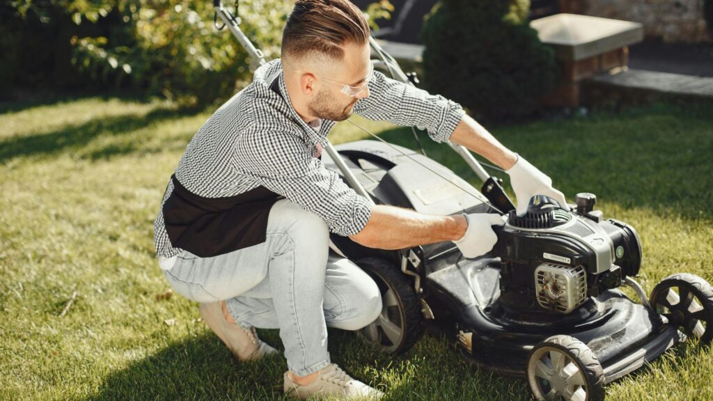 Homem ajustando o motor de um cortador de grama a gasolina sobre gramado residencial, simbolizando a potência e mobilidade do cortador de grama para terrenos irregulares e de grandes áreas.