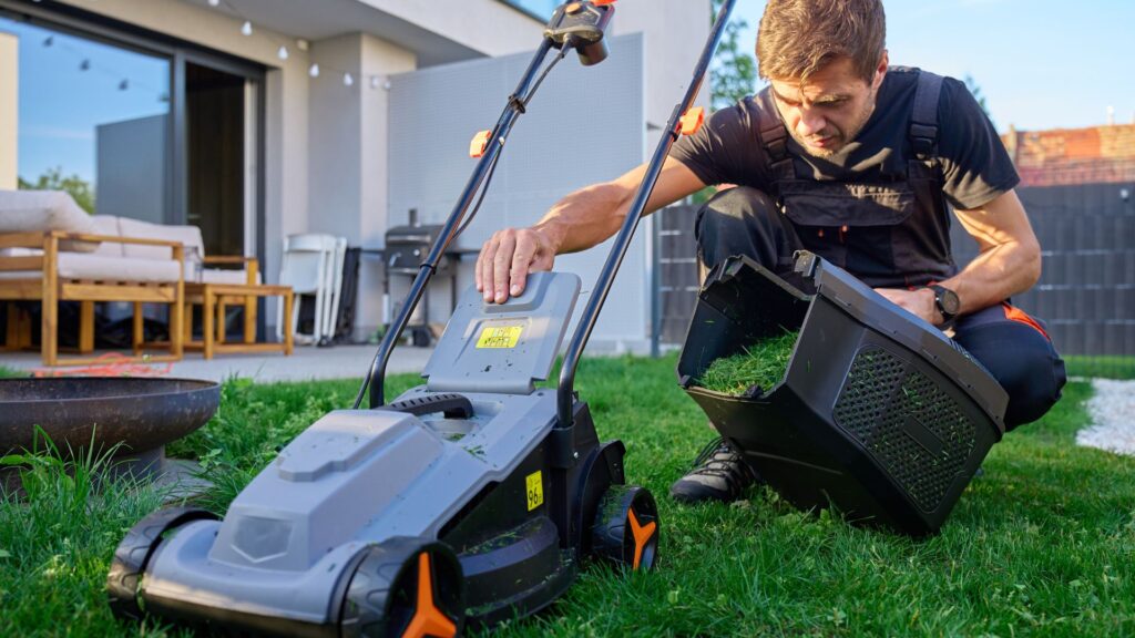 Homem usando cortador de grama com coletor em jardim residencial.