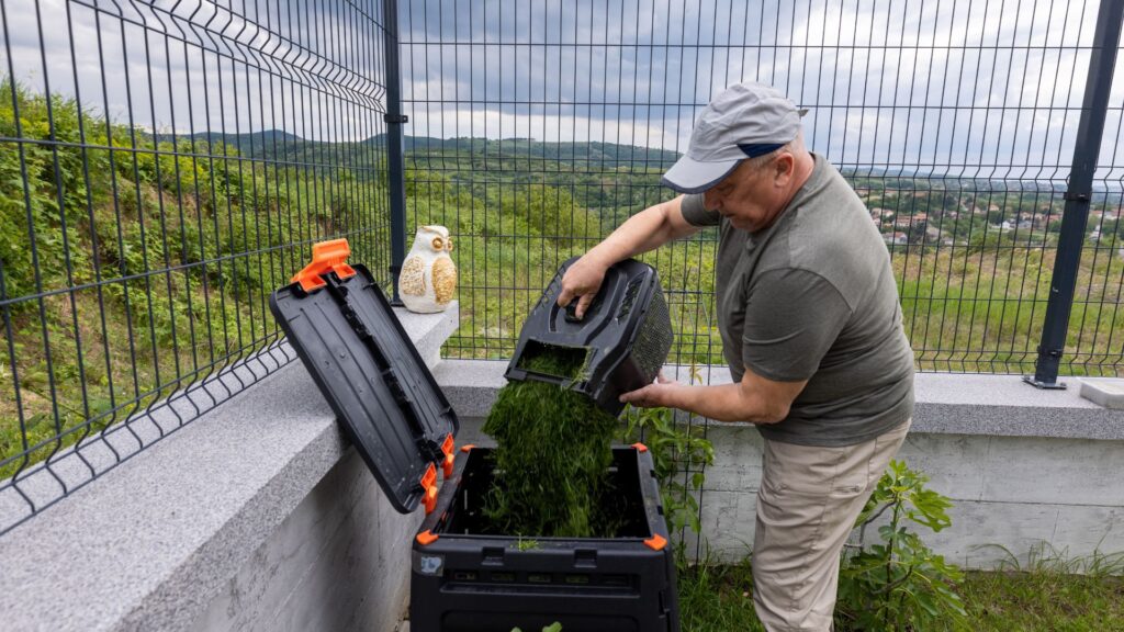 Homem despejando grama cortada do coletor em composteira doméstica.
