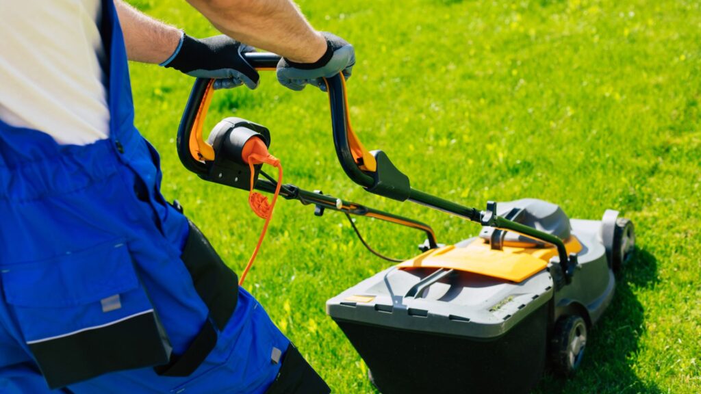 Homem operando cortador de grama elétrico com coletor em gramado verde