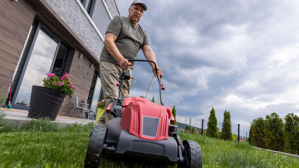 Homem utilizando um cortador de grama em terreno irregular, mostrando como o equipamento adequado torna o corte mais fácil, seguro e prazeroso, mesmo em áreas inclinadas.