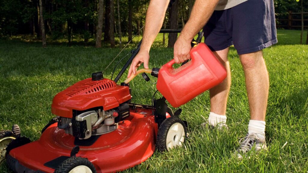 Pessoa abastecendo um cortador de grama a gasolina, representando o processo de lubrificação e troca de óleo essencial para manter o bom funcionamento e prolongar a vida útil do motor.