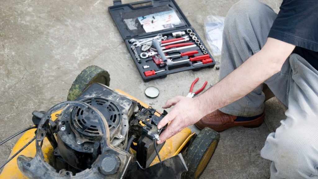 Homem realizando manutenção em um cortador de grama para terrenos irregulares, com ferramentas abertas ao lado, representando a importância dos cuidados regulares com o equipamento para garantir desempenho e durabilidade.