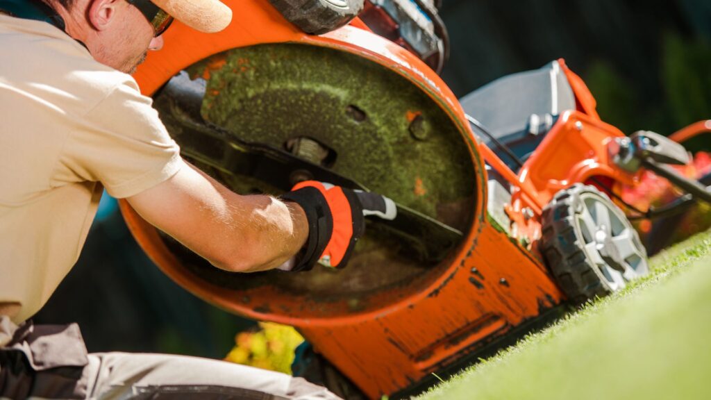 Homem com luvas realizando a manutenção da lâmina de um cortador de grama