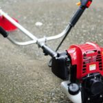 roçadeira a gasolina com motor vermelho e guidão duplo posicionada no chão pronta para uso