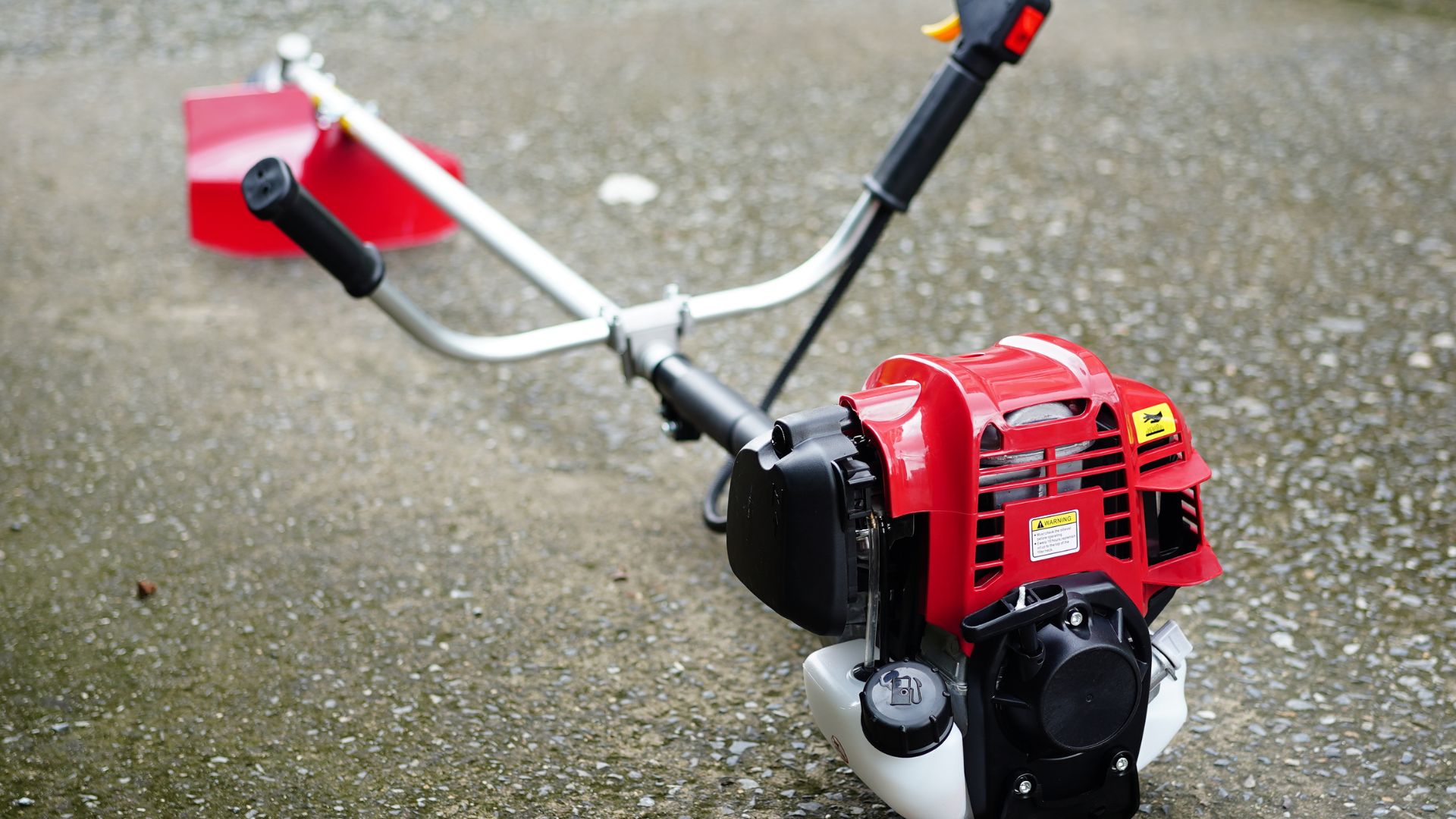 roçadeira a gasolina com motor vermelho e guidão duplo posicionada no chão pronta para uso