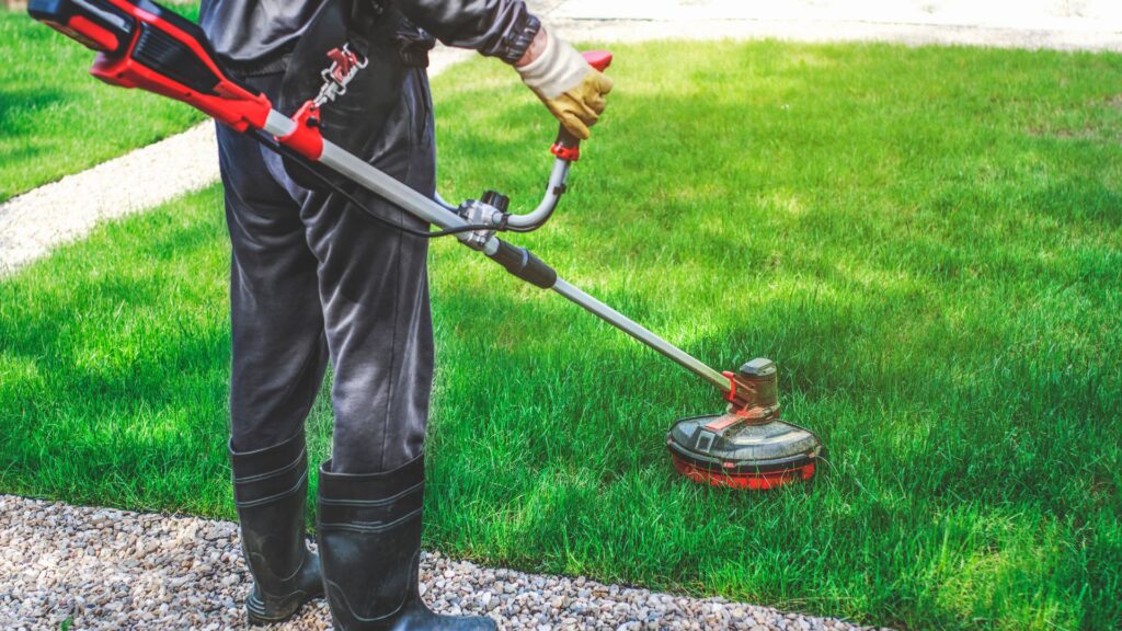 jardineiro utilizando roçadeira para cortar grama alta em área residencial