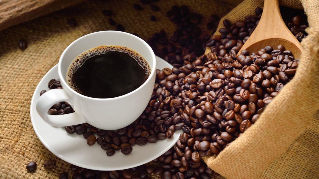 Xícara de café preto ao lado de grãos torrados recém-colhidos.