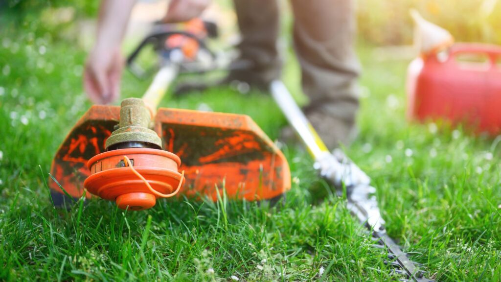 Cabeçote de roçadeira alaranjada apoiada sobre a grama durante manutenção de jardinagem