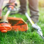 Cabeçote de roçadeira alaranjada apoiada sobre a grama durante manutenção de jardinagem