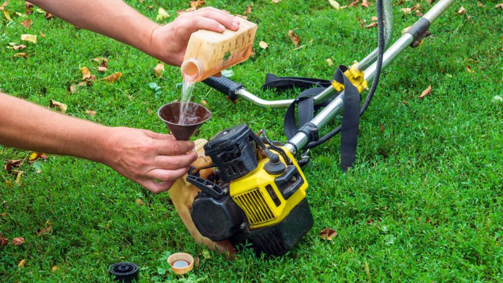 Pessoa abastecendo roçadeira a gasolina em gramado verde, preparando o equipamento para cortar mato alto e terrenos extensos.