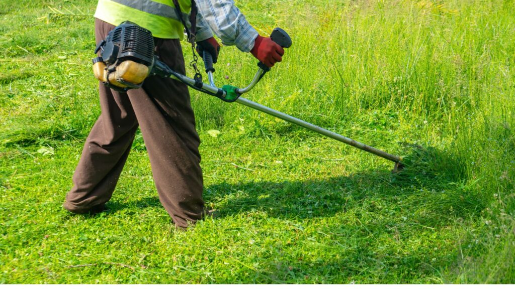 Homem utilizando uma roçadeira costal a gasolina em gramado alto e terreno irregular, demonstrando a precisão e versatilidade do cortador de grama para terrenos irregulares com obstáculos e desníveis.