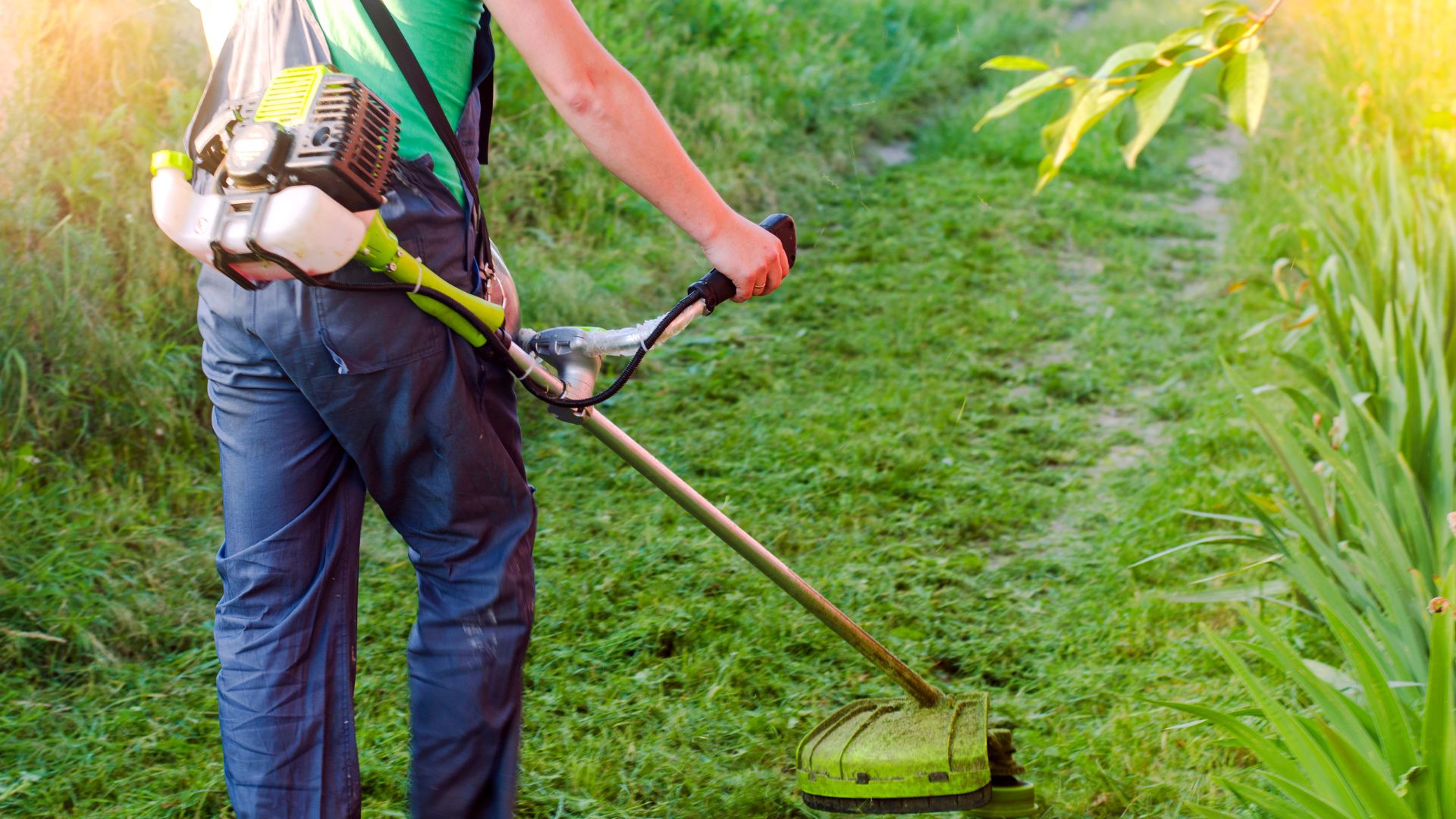 Pessoa utilizando uma roçadeira lateral para cortar grama em jardim verde