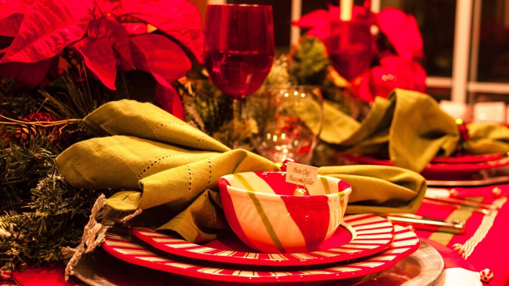 Mesa de jantar decorada com poinsettias vermelhas, pratos e taças natalinas, destacando o uso da flor de Natal em centros de mesa elegantes.
