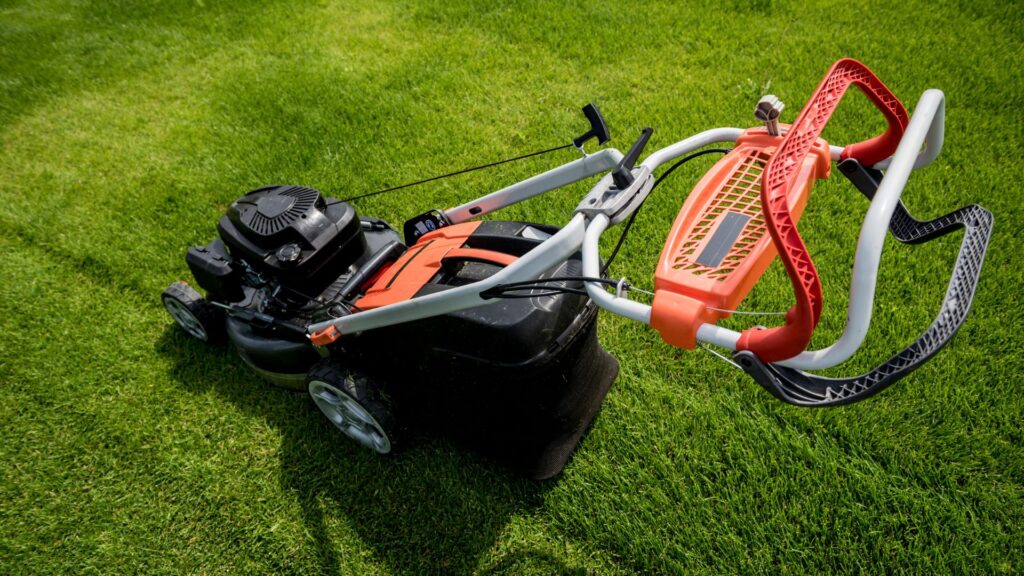 Cortador de grama automático com sistema de tração em destaque, mostrando alavancas e cabos de controle no guidão.