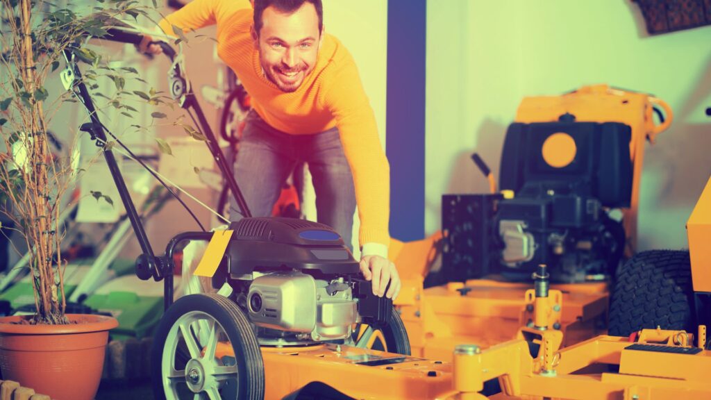 Homem verificando o motor de um cortador de grama automático em loja, ilustrando manutenção preventiva do equipamento.