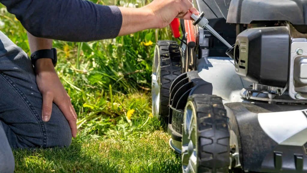 Pessoa verificando o nível de óleo em um cortador de grama com motor quatro tempos, prática essencial de manutenção preventiva.